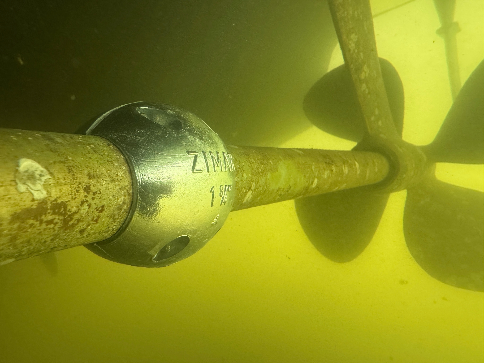 Underwater Boat Shaft Zinc Anode Replacement, Close‑up underwater view of a boat propeller shaft with a new zinc anode installed in front of the propeller to protect running gear from corrosion.